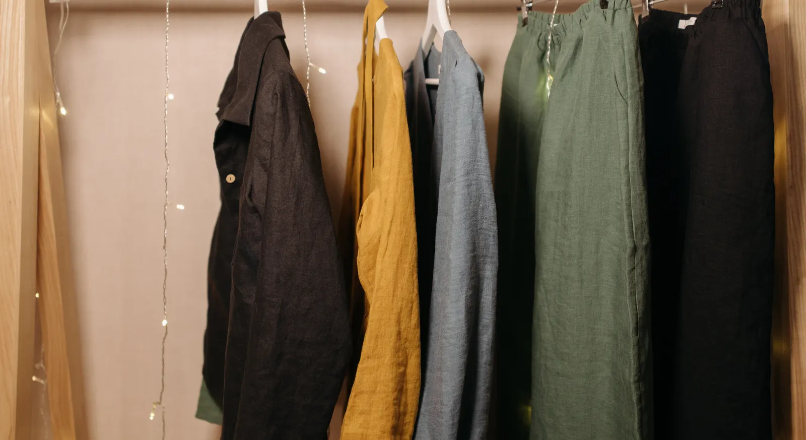 Linnen kleding aan een houten rail tegen een zandkleurige muur